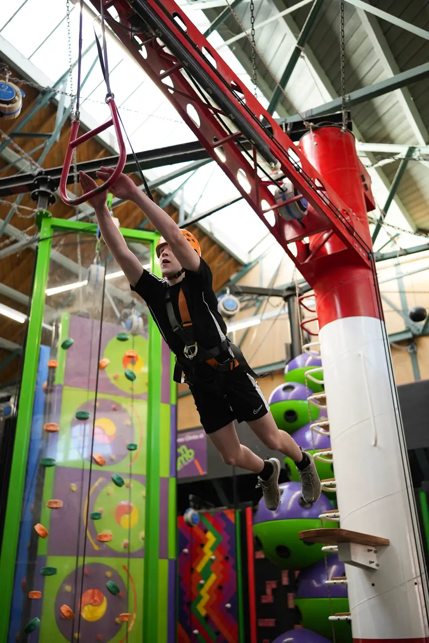 A boy about to grab the suspended trapeze of the Leap of Faith challenge at Clip 'n Climb